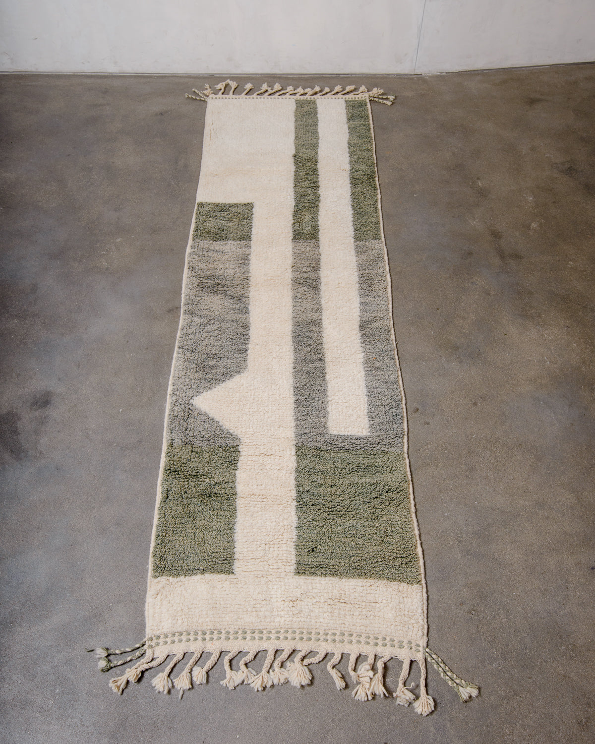 Berberlin Berber runner rug in cream and sage green wool, laying flat on cement floor.